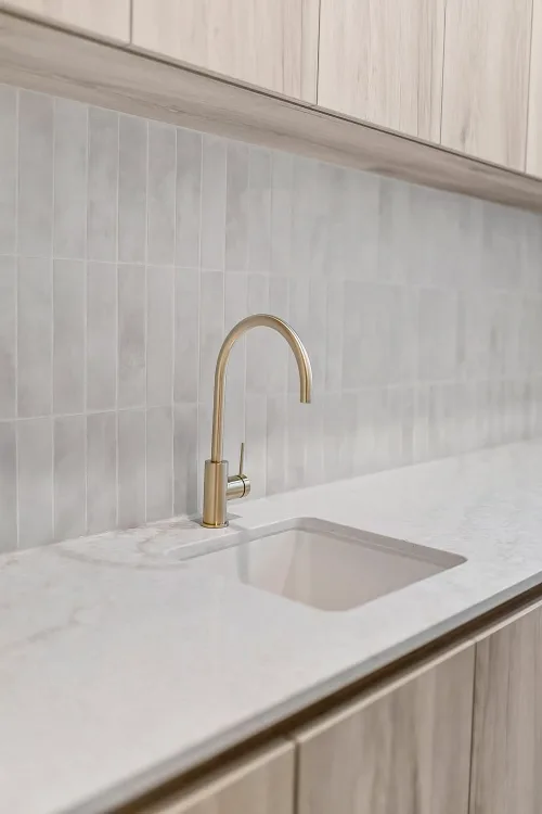 Stone benchtop, brass tapware and pale joinery from a Balo Homes kitchen
